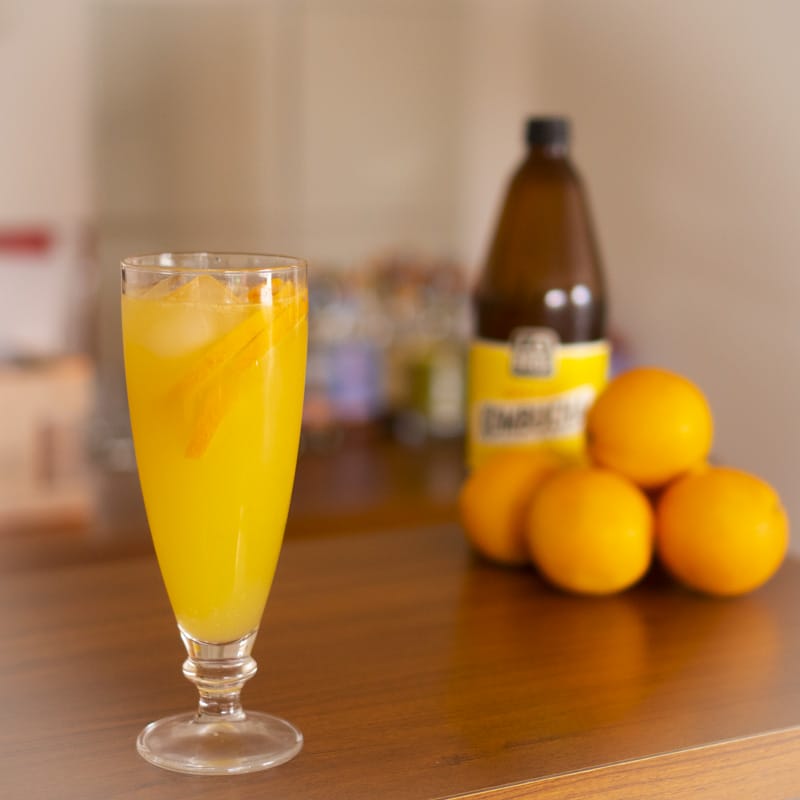 kombucha orange fizz mocktail with blurry oranges and bottle behind